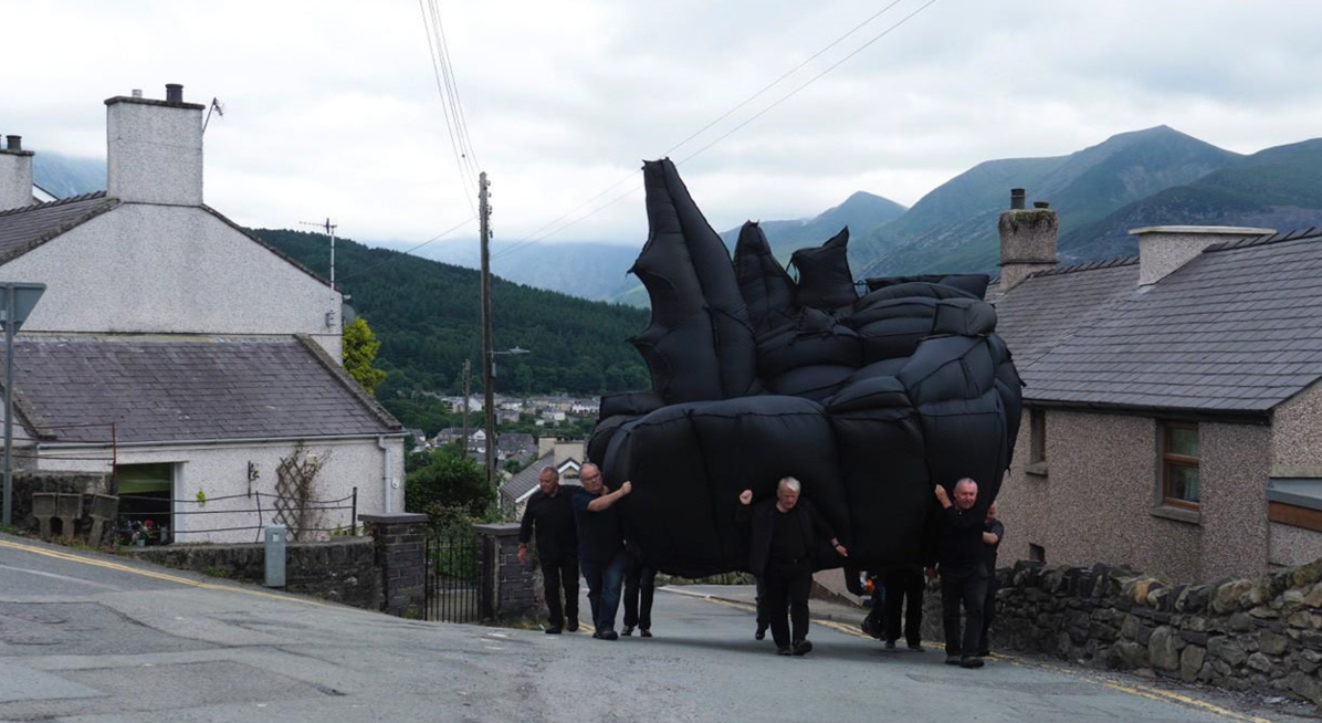 A group of men carrying a large inflatable sculpture up a hil